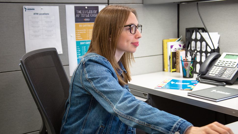 Pelican Team Member with Glasses and Denim Jacket Working on a Computer